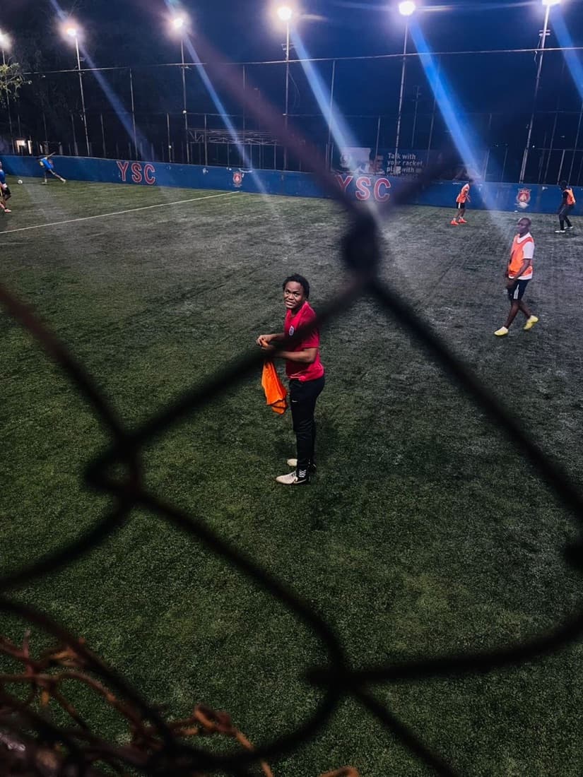 Seen through the pitch-side chain-link fence, holding a bib.