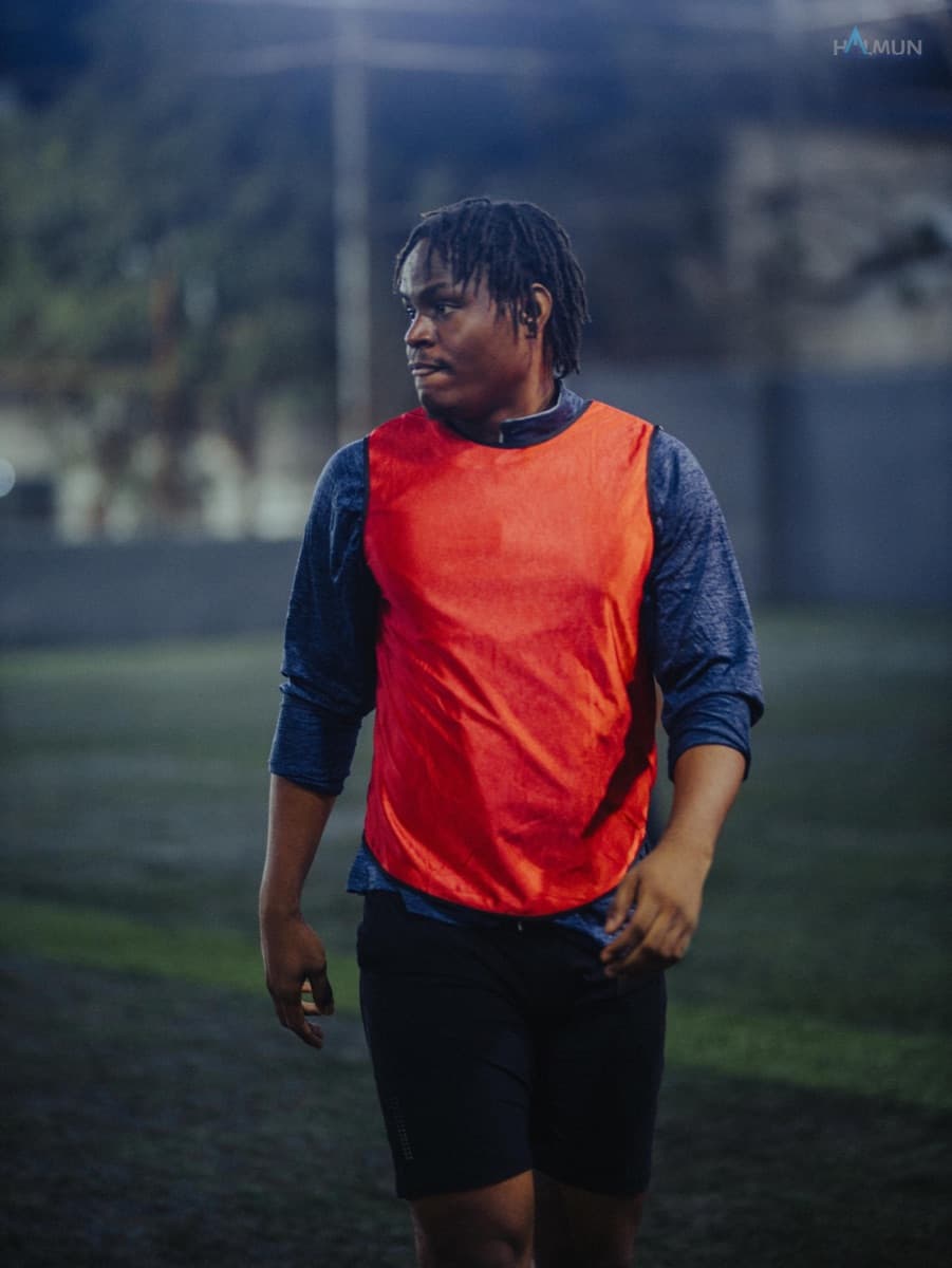 Walking the pitch in an orange training bib, shallow focus.