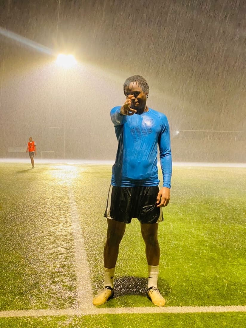 Pointing at the camera mid-downpour under a floodlight.
