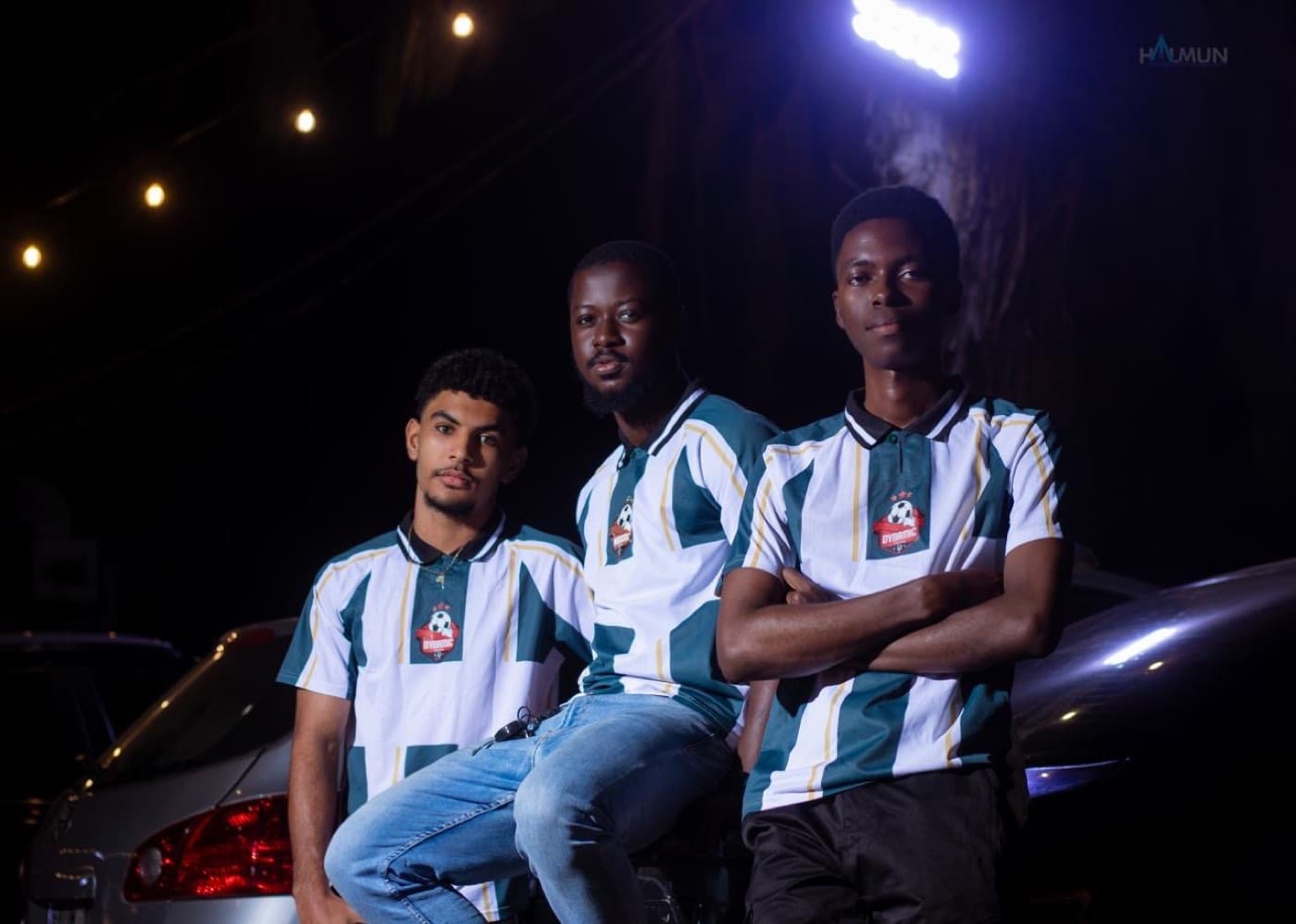 Three players in kits leaning on a car under string lights.