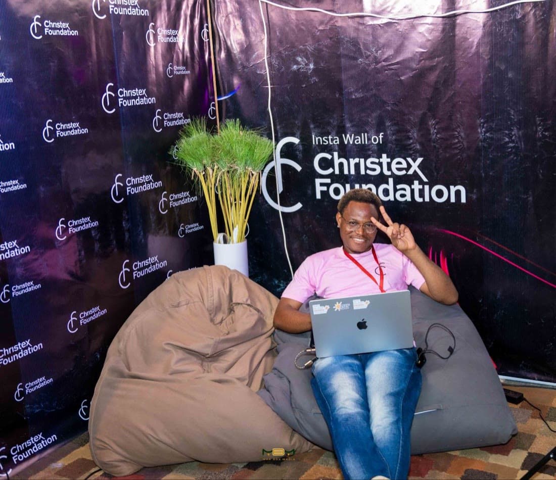 On a beanbag at the Christex Foundation insta wall, peace sign up.