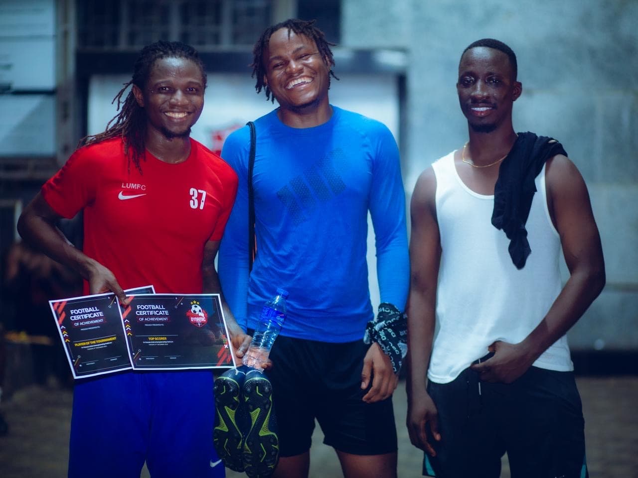 Three friends smiling with football certificates and a medal.