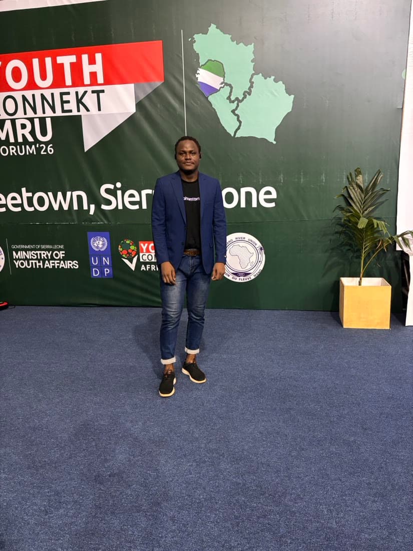 Standing full-length in a blazer at a conference backdrop.