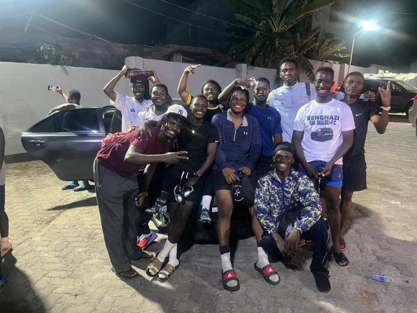The whole crew crowded around a car after the game, phones out.