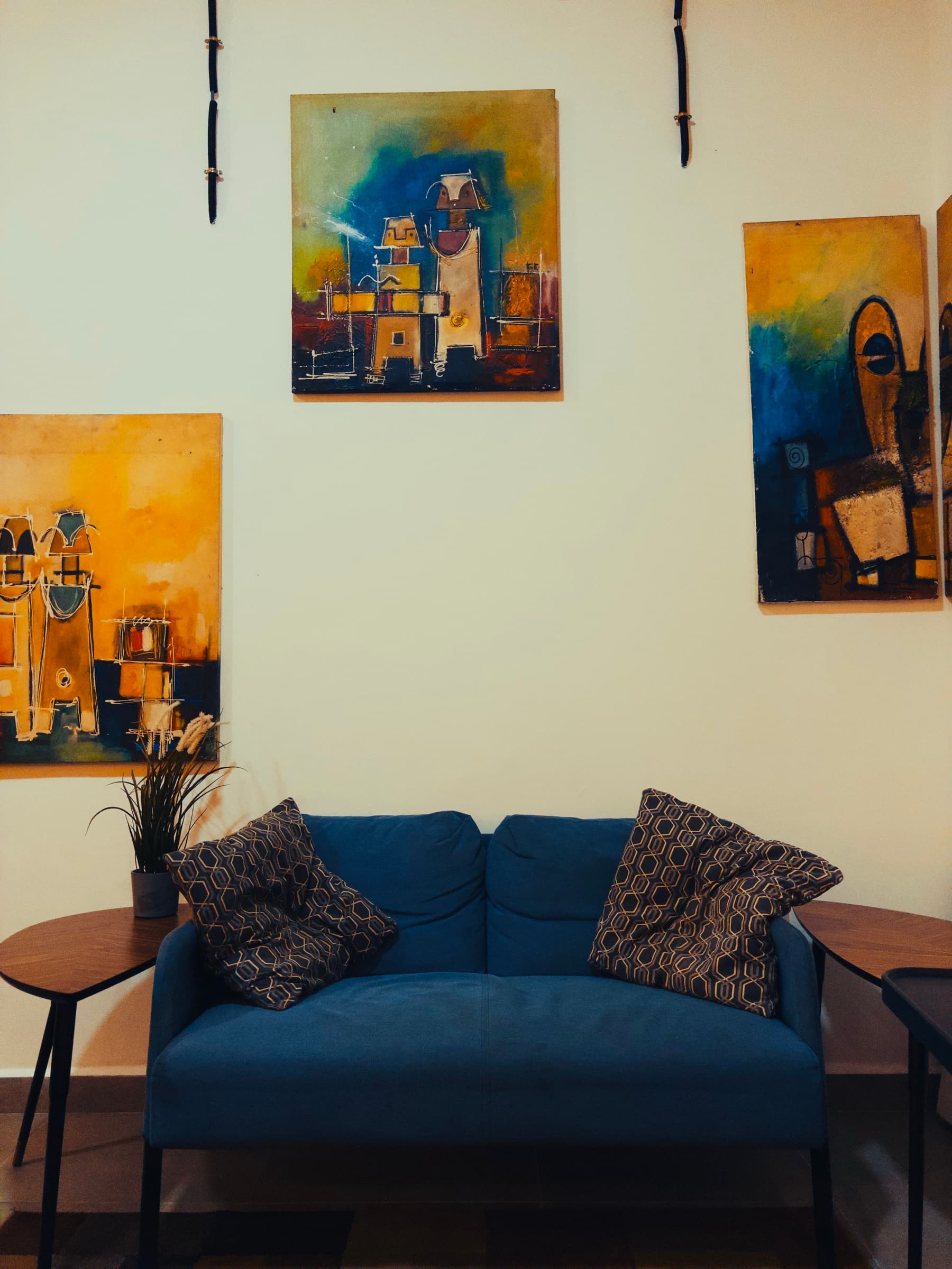 A blue two-seater sofa beneath a wall of paintings, both seats open.
